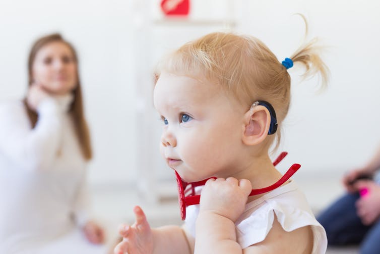 woman in back with young child in foreground wearing hearing device